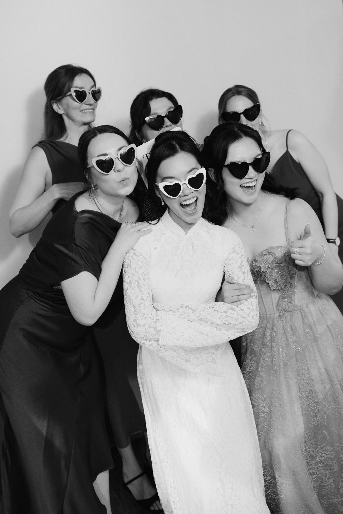 Bräute-Crew in Schwarzweiß mit Herz-Sonnenbrillen posiert vor Fotobox bei Hochzeit